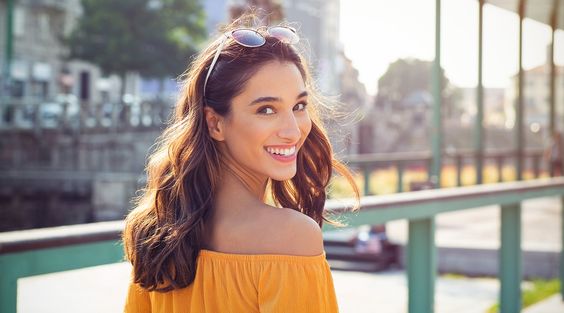 Happy latin woman looking behind while walking on street. Beautiful young woman enjoying vacation during summer. Cheerful girl in smart casual walking and looking at camera while smiling.